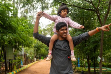 Sevgi dolu bir baba parkta yürürken kızını omuzlarında taşır. Kızı gülüyor, gülüyor ve babası parkta bir şey gösteriyor.