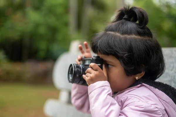 stock image A young girl with pigtails and a big smile holds a DSLR camera up to her eye. She is looking through the viewfinder, focused on taking a picture.