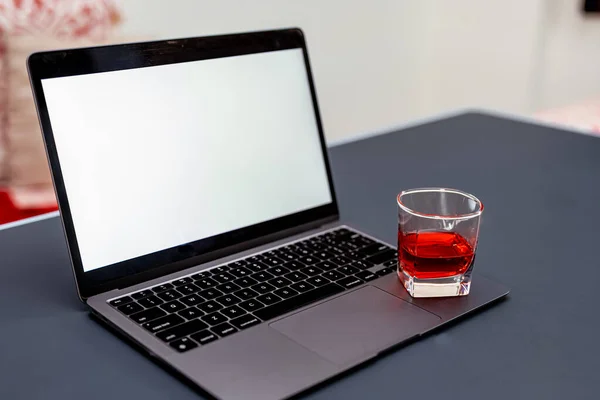 Bir bardak kırmızı şarap dizüstü bilgisayarın üstünde duruyor, iş ve zevk arasında bir denge olduğunu gösteriyor. Görüntü çeşitli amaçlar için uygundur.