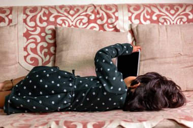 Küçük tatlı bir kız kanepede uzanıyor ve tablete bakıyor. taşınabilir bağımlılık kavramı