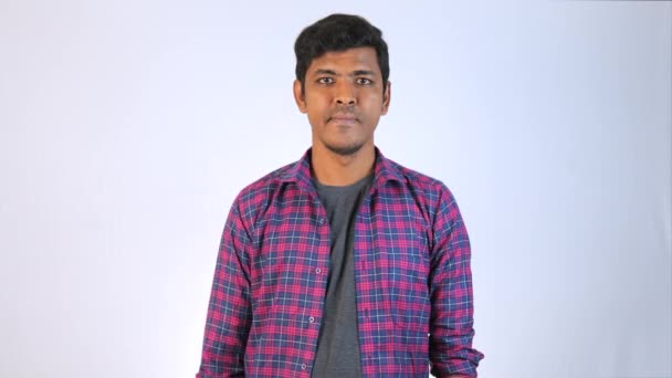 友好的な表情を持つ若いインド人男性は 明白な背景の前に立って スーパー の看板に2本の指を保持しています カジュアルなシャツとジーンズを着ています — ストック動画