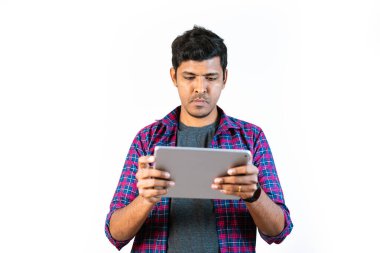 20 'li yaşlarda genç bir adam elinde bir tablet bilgisayar tutuyor. Beyaz bir arka planın önünde duruyor.