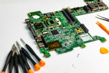 Etrafı çeşitli alet çantalarıyla çevrili bir laptop ana kartı.