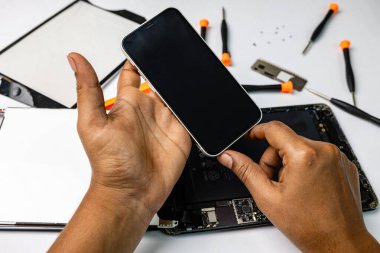 Yetenekli teknisyen çeşitli araç gereçlerle bir cep telefonunu ve tableti dikkatlice tamir ediyor.