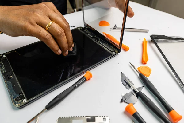A technician carefully cleans a tablet for repair using a variety of tools
