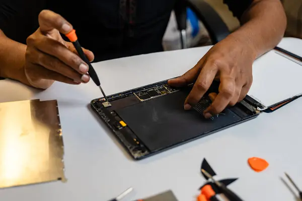 A technician is carefully repairing a tablet with a variety of tool kits. They are using a screwdriver to open the tablet