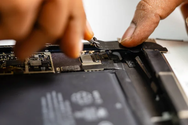 technician carefully removes the damaged ribbon from a tablet using specialized tools