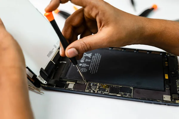 A professional technician is carefully repairing a tablet with a variety of tools