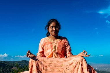 Hintli bir kadın, görkemli bir dağ zirvesinde meditasyonla teselli ve huzur arar.