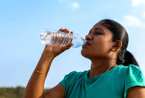 A young woman takes a satisfying sip from a water bottle
