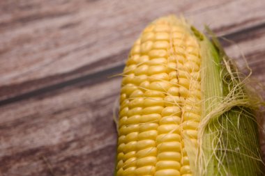 Kırsal bir ahşap masada sergilenen canlı yeşil kabuklu taze mısırdan yapılmış yakın plan bir fotoğraf.