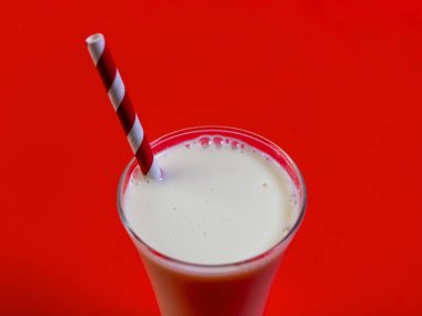 Kırmızı ve beyaz şeritli kamışla kaplı, uzun bir bardakta, kalın ve kremalı bir milkshake.