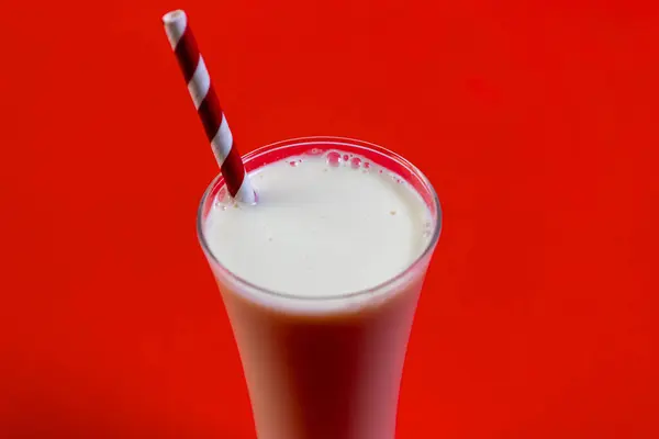 Pipetle bardakta canlandırıcı bir milkshake, canlı kırmızı bir arka planda..