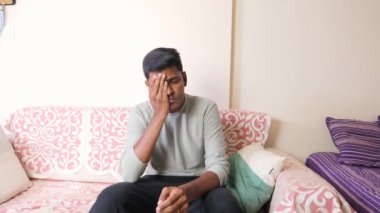 Düşünceli bir Hintli adam bir kanepede tek başına oturur, derin düşüncelere dalmış, ya da belki de bir anlık üzüntü hisseder..