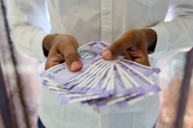 Modern bir ofisteki temiz ve düzenli bir masada işadamlarının elleri titizlikle 100 rupilik banknotları sayıyor..