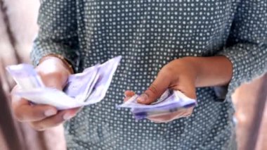 Güney Asyalı bir kadının yakından çekilmiş fotoğrafı dikkatle bir yığın 100 rupilik Hint banknotunu sayıyor.