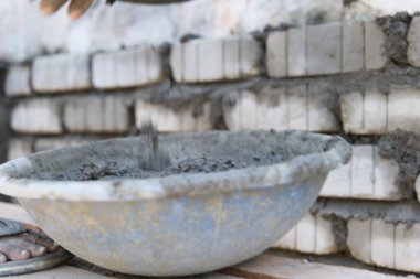 İnşaat işçisinin güvenlik teçhizatı ile yakından çekilmiş bir fotoğrafı. İnşaat alanındaki bir kovadan titizlikle çimento harcı dökülüyor.