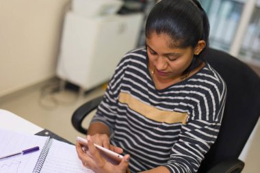 Ofis masasında dijital tablet üzerinde çalışan odaklanmış genç bir kadın. Yan görünüm.