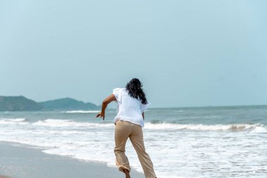 A joyful women sprints toward the ocean on a sunny beach day, capturing the essence of carefree seaside adventures clipart