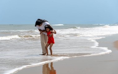 Anne ve kızı, güneş sakin kumsalda batarken yürekten bir kucaklaşmayı paylaşıyor. Dalgalar nazikçe kumu öpüyor, huzurlu bir an yaratıyor.