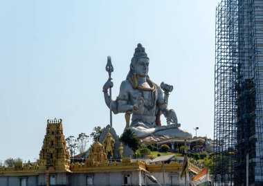 Lord Shiva 'nın heykeli, çoklu kolları ve sakin bir ifadeyle, canlı mavi gökyüzüne karşı bir tepenin üzerinde duruyor. Bu ikonik dini sembol barışı ve maneviyatı çağrıştırıyor..