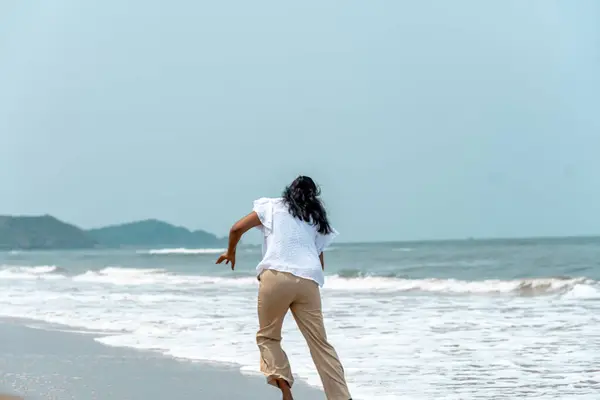 Stock image A joyful women sprints toward the ocean on a sunny beach day, capturing the essence of carefree seaside adventures