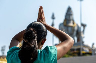 Geleneksel Anjali Mudra 'da bir kişi heybetli bir Hindu tanrısı heykeli önünde dua eder. İnşaat iskelesi tadilatta ipuçları veriyor. Cinayet SavaşıName