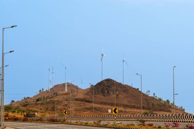 Uzak bir tepenin üstünde rüzgâr türbinleri olan sakin otoyol sahnesi sürdürülebilir enerjiyi simgeliyor..