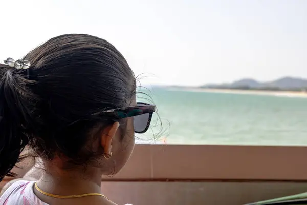 stock image A Child is captured from behind, out at a body of water. The focus on the individuals hair tied back and the edge of sunglasses evokes a sense of peaceful.