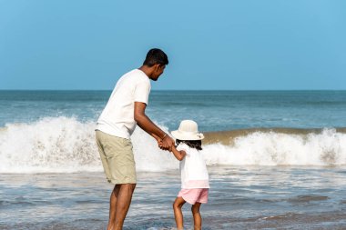 Güneş ufkun altına batarken, sadık bir baba, sakin sahil boyunca genç kızıyla el ele yürür. Ayak izleri kumu işaret ediyor.