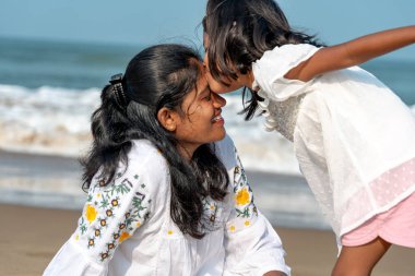 Beyaz giyinmiş üç kişilik bir aile, okyanus dalgalarının kıyısında huzurlu bir anın tadını çıkarıyor.