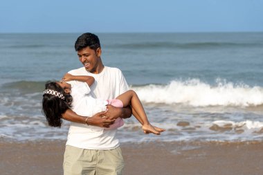 Gök kubbenin altında, kendini adamış bir baba küçük kızını yakınında tutar, çıplak ayaklarıyla sıcak kuma batar..