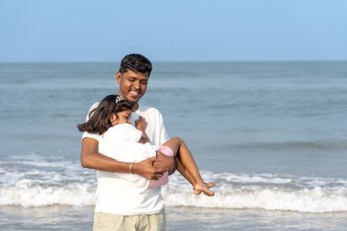 Sevgi dolu bir baba, kızına yakın durur, parmakları sıcak kuma batar. Dalgalar kıyıya vurur Deniz kıyısında değerli bir anı paylaşırken.