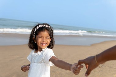 Huzurlu bir sahil sahnesinde bir anne ve genç kızı el ele tutuşurken, kahkahaları okyanus esintisi tarafından taşınırken görüntülenir. Sevgiyle dolu değerli bir bağ anı.