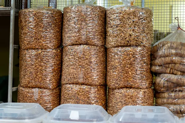 Hareketli bir market, taze toplanmış badem kutularını inceliyor. Sıcak güneş ışığı açık vitrinden süzülerek yüzlerine altın bir parıltı saçar..