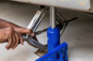 Bu yakın planda, bir çift el, bir şişe krikosunu ve makas krikosunu ustalıkla, bakım için bir arabayı kaldırıyor. Bu sağlam aletler otomotiv tamirinde çok önemli bir rol oynar.