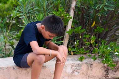 Genç bir çocuk taştan bir çıkıntıda tek başına, yemyeşil bir alanda dalgın dalgın dalgın oturuyor. Kasvetli ruh hali onların iç düşüncelerini yansıtır..