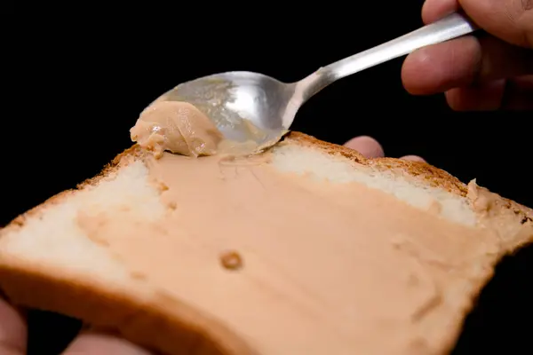 Stock image A close-up photo of a heaping spoonful of peanut butter being deposited on a slice of toast.