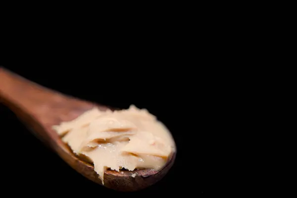 stock image This image is about close up of a wooden spoon with peanut butter on a black background