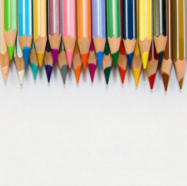 Beyaz arka planda düzgünce hizalanmış renkli kalemlerin üst görünümü. Sanat, yaratıcılık ve eğitim temaları için mükemmel.