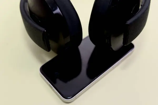 Modern siyah kulaklıkları yakın plan, parlak bir telefon üzerinde dinleniyor, minimalist bir ışık arka planında..