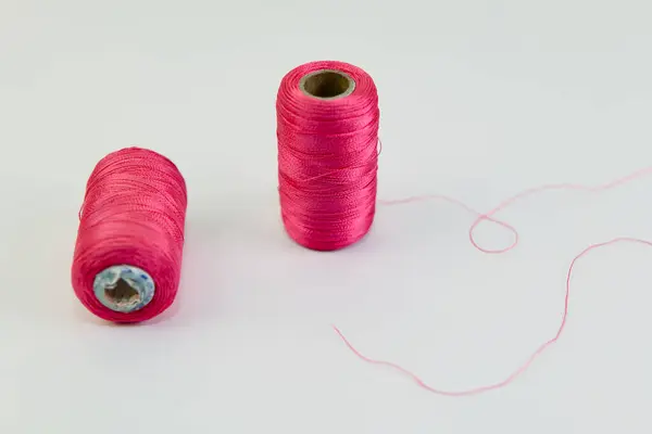İki canlı pembe iplik makarası beyaz bir arka planda uzanır, tek bir tel şakacı bir şekilde takip eder. Yaratıcı bir fırtınayı dikmeye hazır?