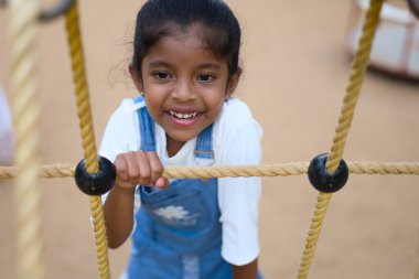 A young girl beams with happiness while playing on the monkey bars, embracing the joy of childhood. clipart