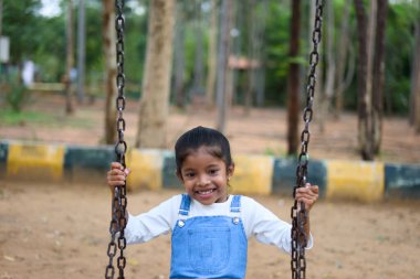 Parkta salıncakta süzülen ve çocukluğun saf mutluluğunu yakalayan genç bir kız neşeyle ışıldıyor..
