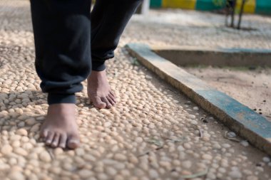 Yalın ayakların yakın çekimi pürüzsüz taşlardan oluşan bir yolda yürüyor, doğaya bir zemin ve bağlantı hissi veriyor..