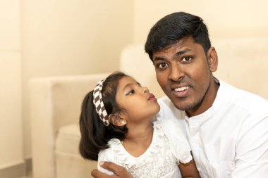 Hintli bir baba ve kız çocuğu fotoğraf çektirmek için birlikte poz veriyorlar.