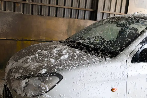 Stock image A car is undergoing a thorough wash inside an automated car cleaning facility, covered in frothy soap as water sprays from various angles.