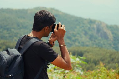 Genç bir maceracı nefes kesen bir dağ manzarasının fotoğrafını çekmek için duruyor..