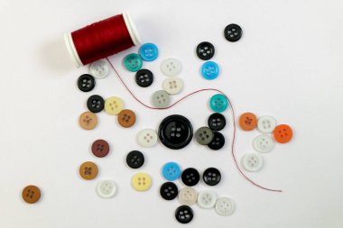 Renkli düğmelerin canlı dağılımı ve temiz beyaz arka planda kırmızı iplik, el sanatları için hazır..