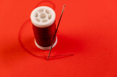 Kırmızı iplik ve iğne, canlı kırmızı arka planda. Dikiş dikmek, terzilik, el işi, DIY. Kopyalama alanı ile minimalist yaratıcı kavram.